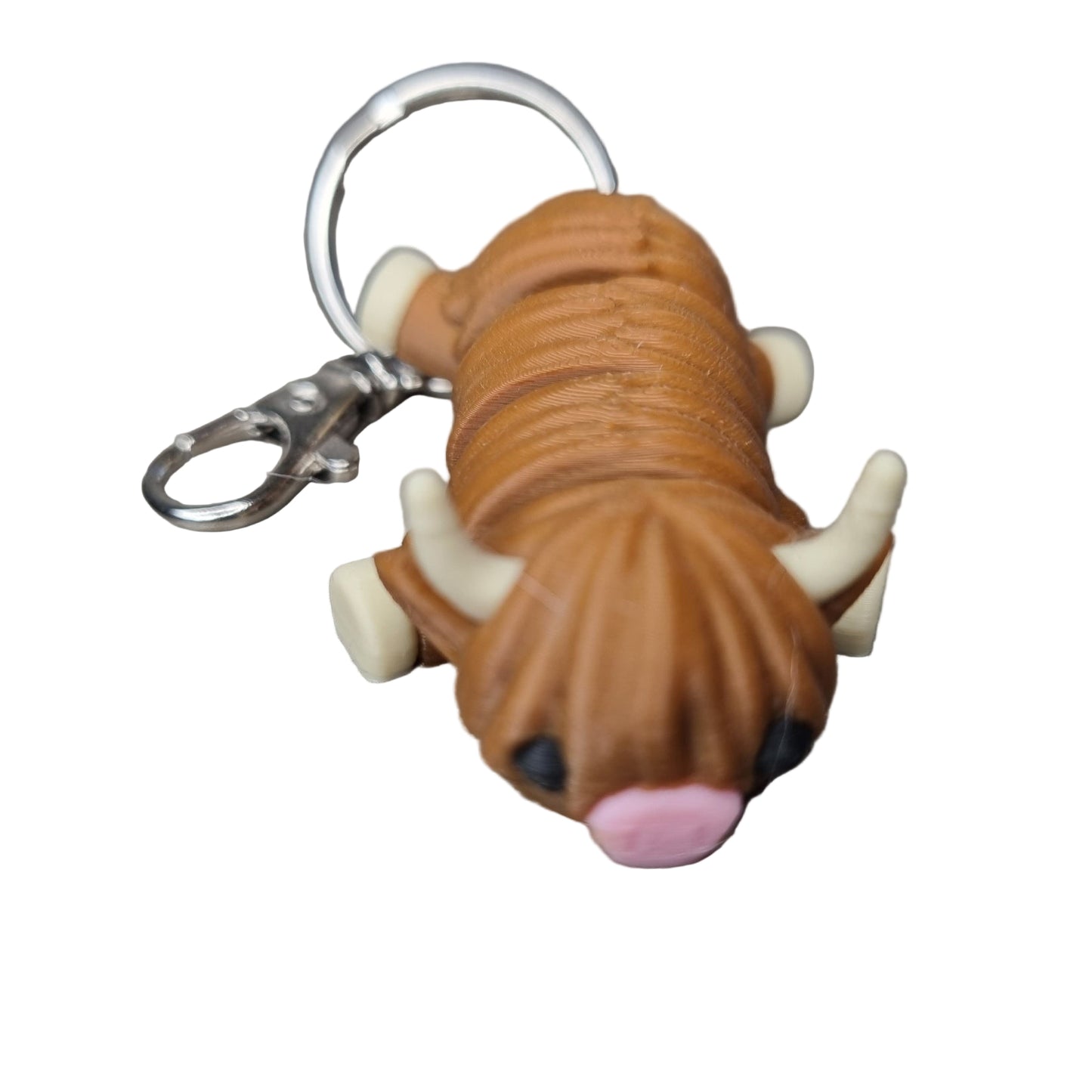 Keychain shaped like a brown highland cow with a pink nose on a wooden surface